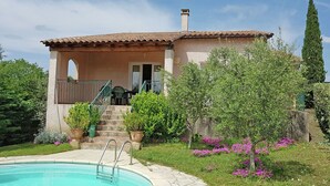 A house with a swimming pool, a covered patio, and a garden with various plants and flowers.