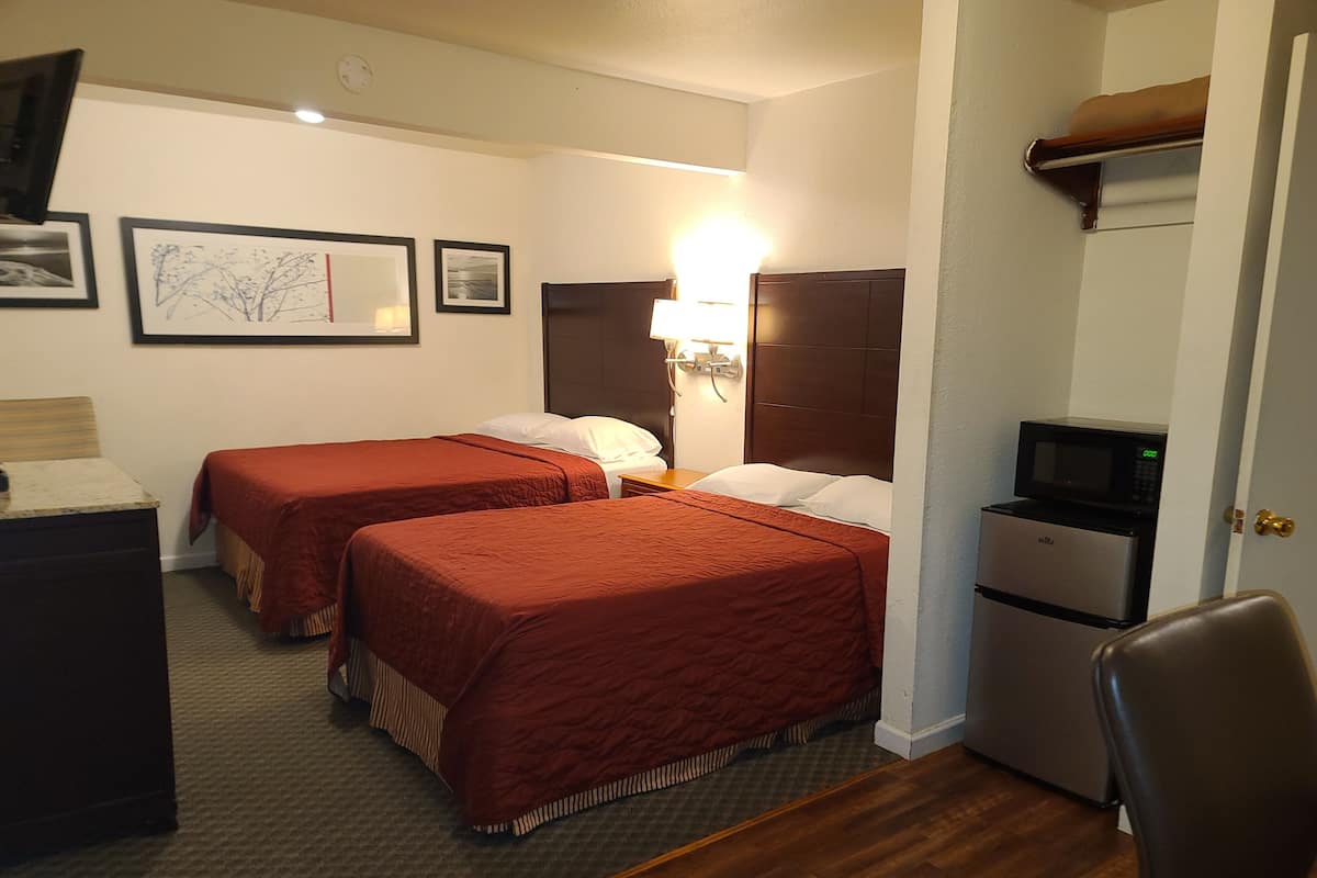 Habitación de hotel con dos camas, un escritorio, una silla, un microondas y un refrigerador pequeño.