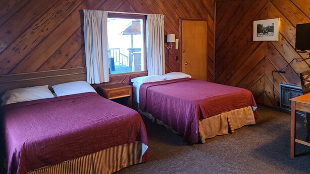 Una habitación con paneles de madera, dos camas, un escritorio y una ventana con cortinas.