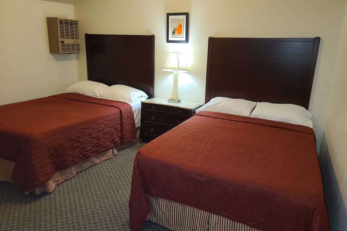 Habitación de hotel con dos camas individuales, una mesita de noche con lámpara, un cuadro en la pared y un equipo de aire acondicionado.