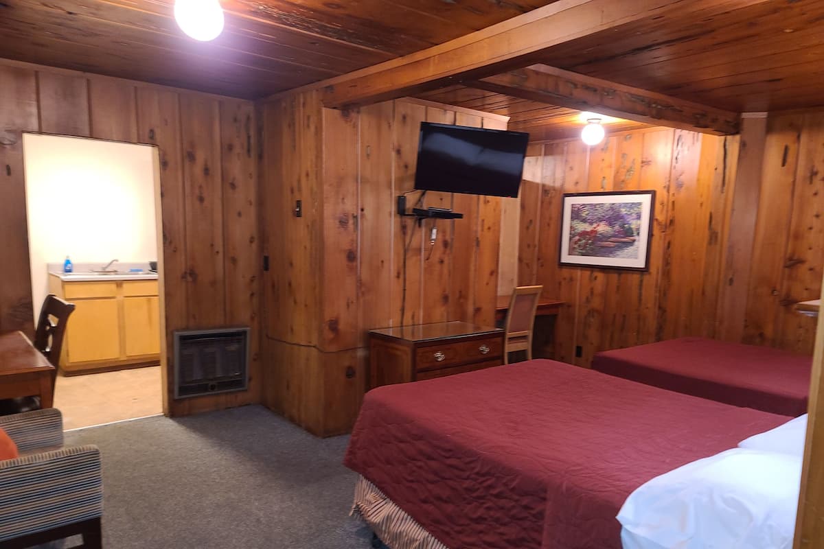 Una habitación con paneles de madera, dos camas, un escritorio, una silla, un televisor y un cuadro en la pared.