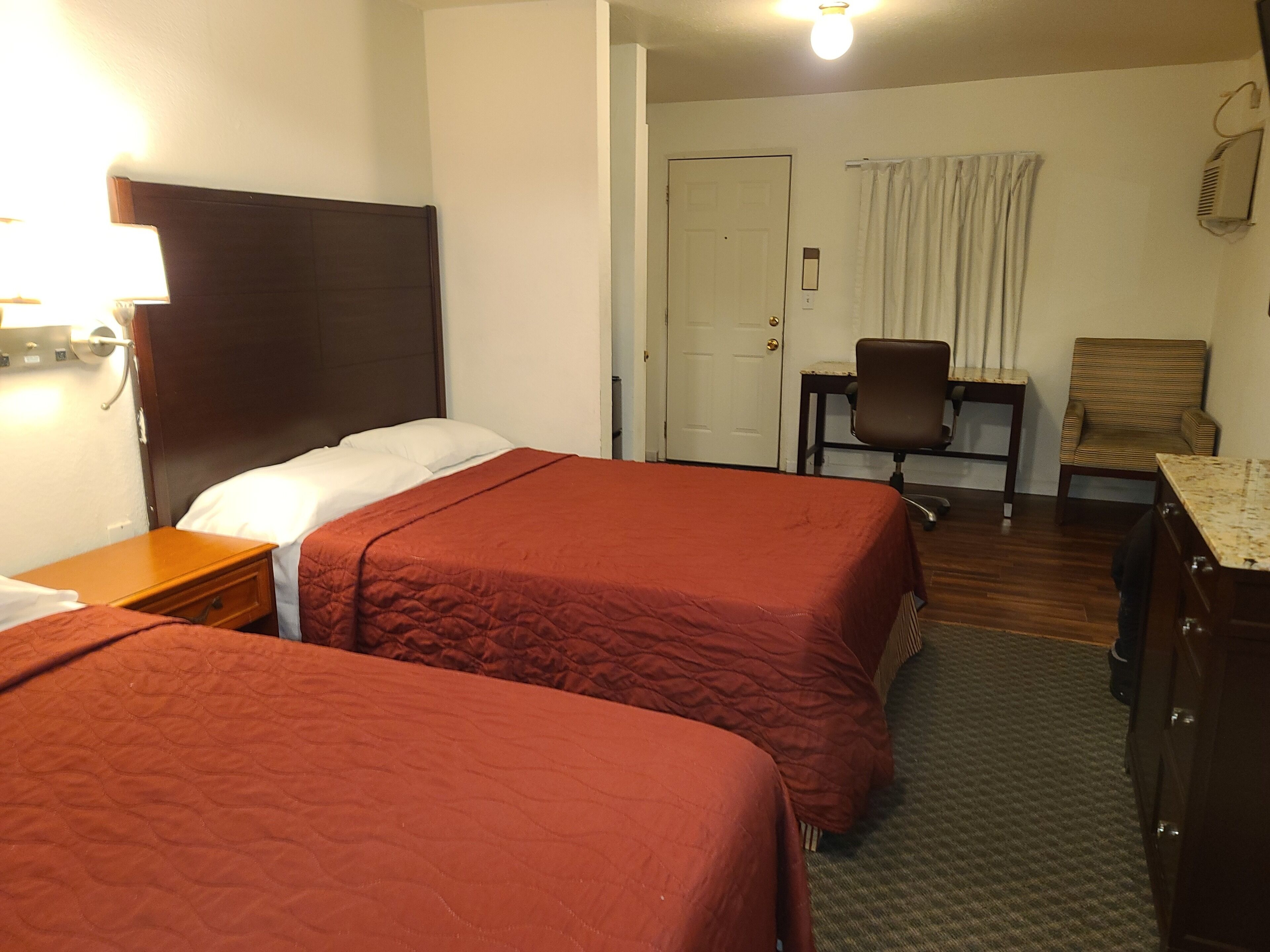 A hotel room with two beds, a desk, a chair, and a dresser.