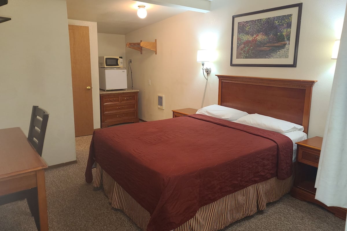 Habitación de hotel con cama, escritorio, cómoda, microondas y un cuadro en la pared.