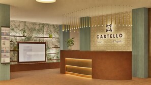 A hotel reception area with a modern design, including a reception desk, a digital screen, and a wall-mounted logo. - Hotel Castello (L'Aquila)