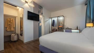 Habitació d'hotel amb un llit gran, televisió de pantalla plana penjada a la paret, escriptori amb una làmpada i armari amb mirall.