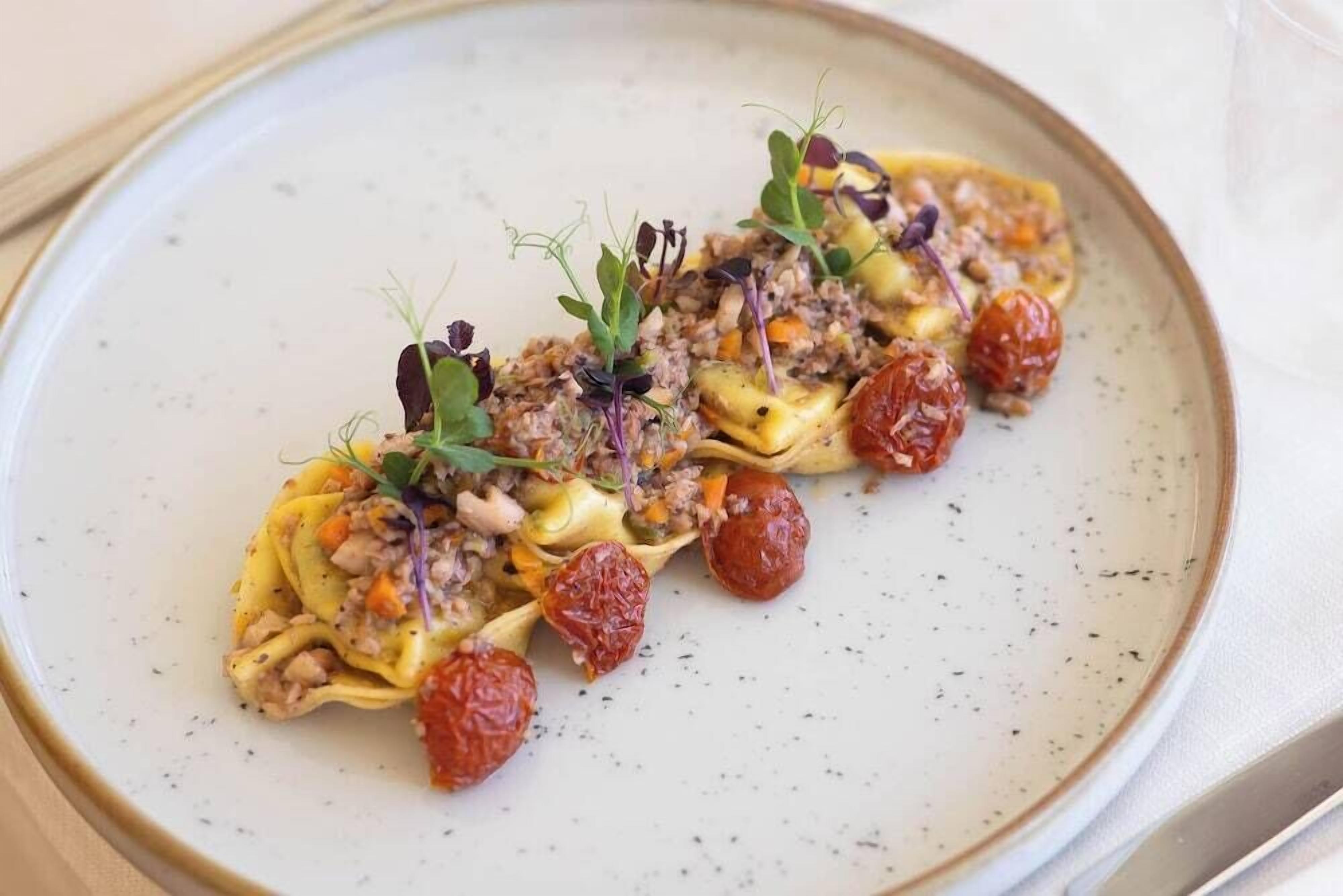 A plate of pasta with a topping of ground meat, vegetables, and garnishes.