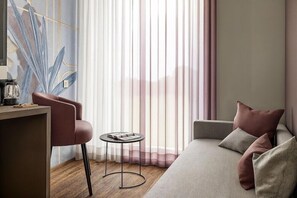 A modern hotel room with a sofa, a small round table, and a chair. - Hotel Castello (L'Aquila)