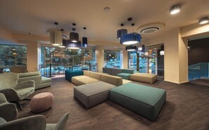 A spacious lobby with multiple seating areas, large windows, and modern pendant lighting. - Hotel Castello (L'Aquila)
