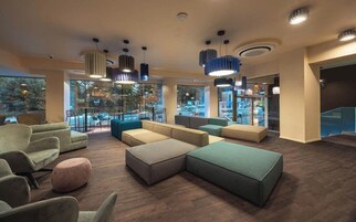 En rummelig lobby med flere siddeområder, store vinduer og moderne hængende lysarmaturer.