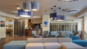 A modern hotel lobby with a seating area, a bar, and a reception desk.