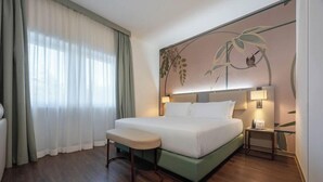 A hotel room with a bed, a bench, a nightstand, and a wall with a plant mural.