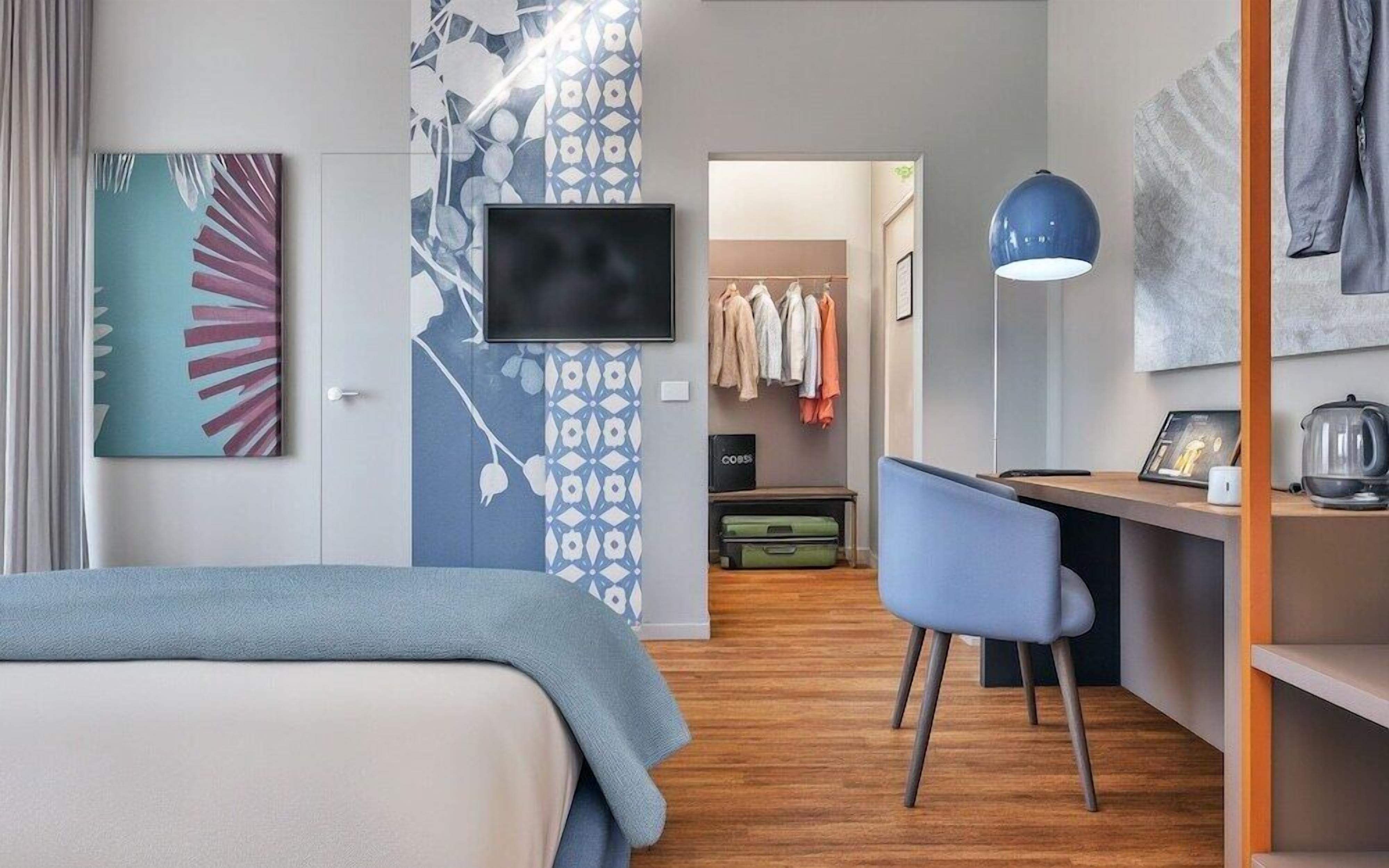 A hotel room with a bed, a desk, a chair, a television, and a wardrobe.