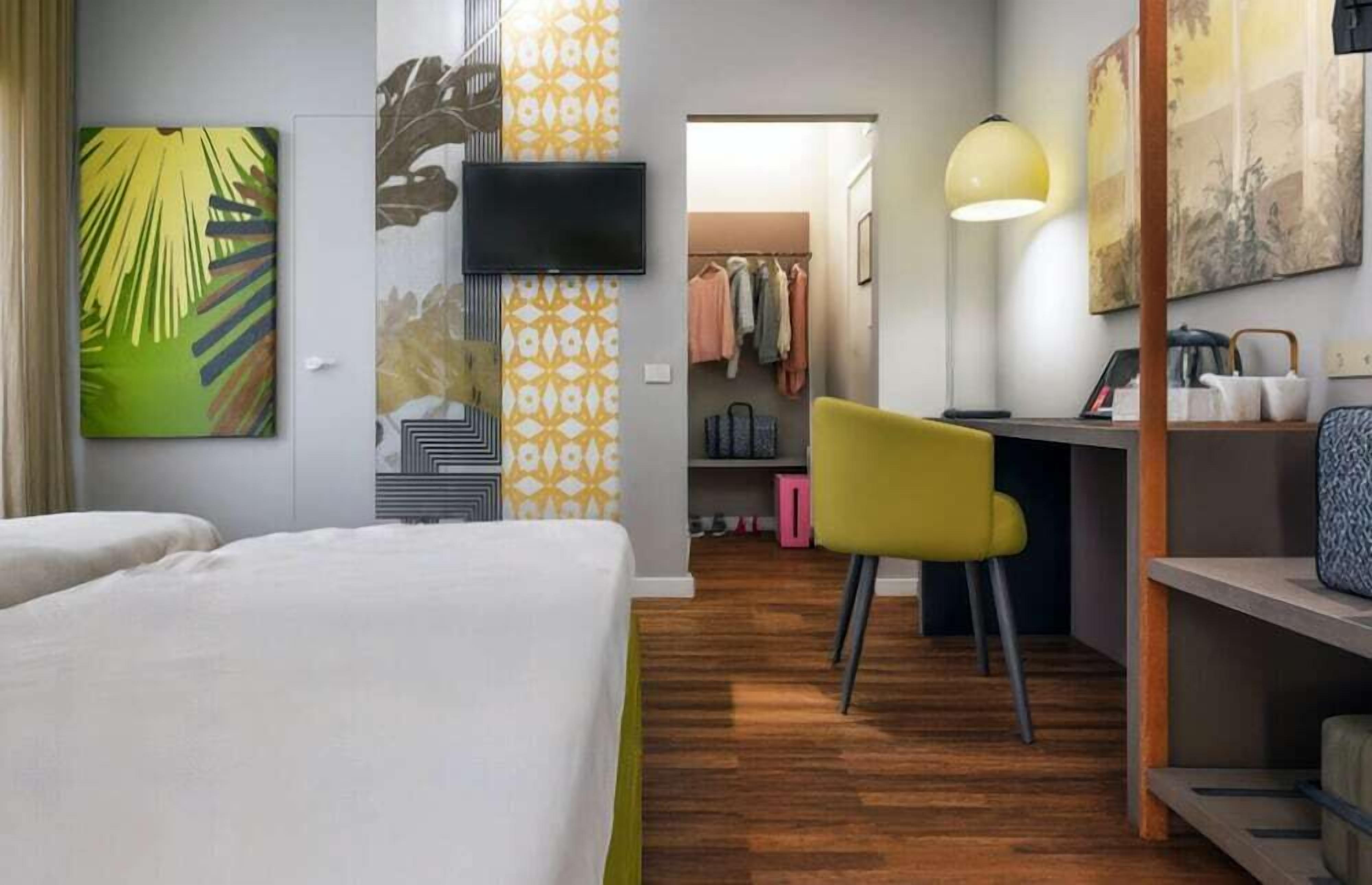 A hotel room with a bed, a desk, a chair, a wardrobe, and a television.