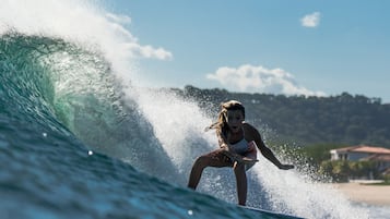 A person surfing a wave with a beach and buildings in the background.