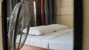 Una cama individual con ropa de cama blanca en una habitación con pared de ladrillo y ventana con cortinas.