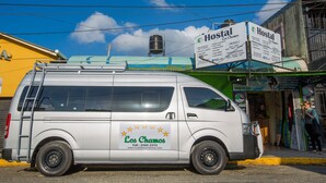 Una camioneta blanca con la marca "Los Chamos" estacionada frente a un hostal.