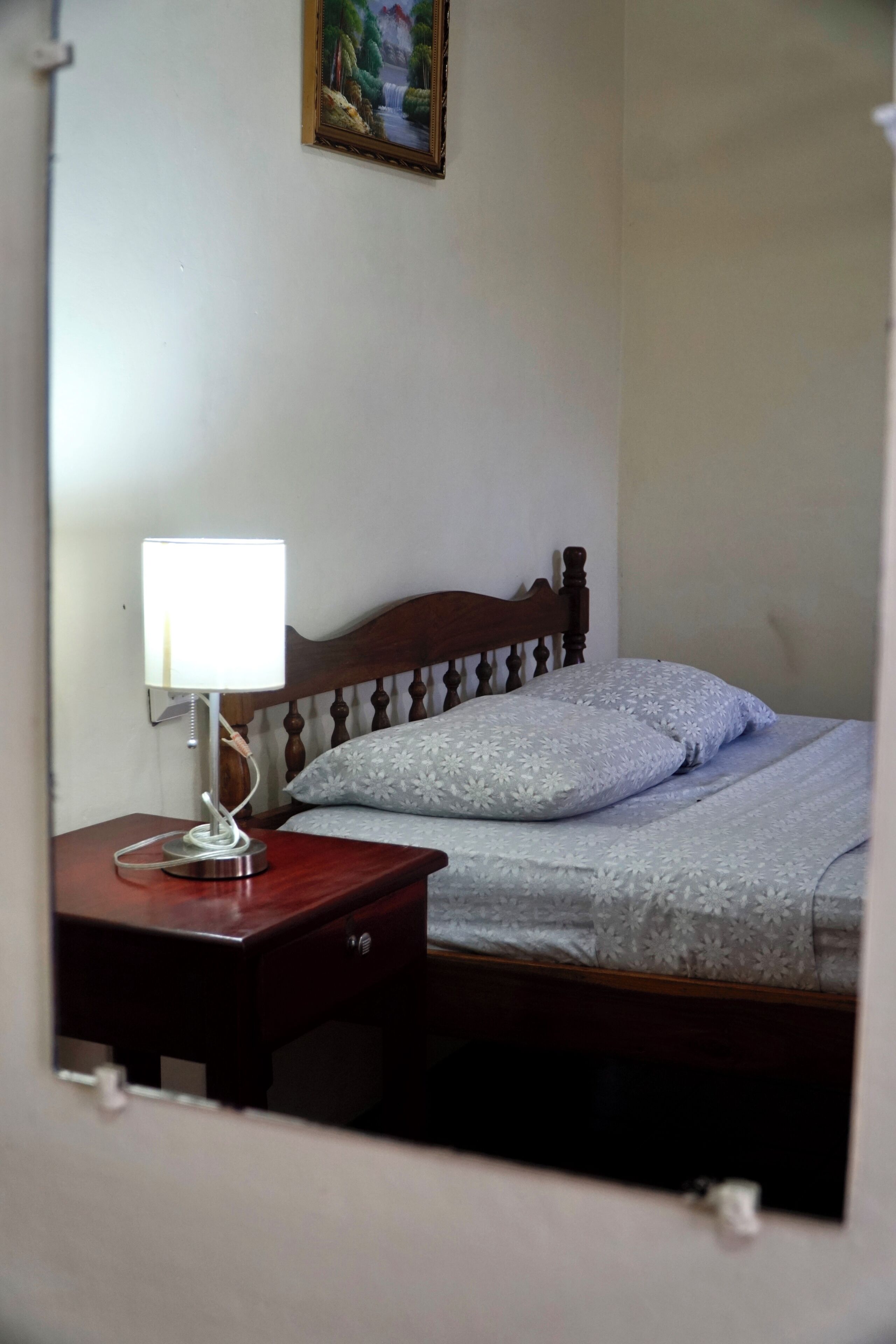 A bedroom with a wooden headboard, a bedside table with a lamp, and a bed with patterned bedding.