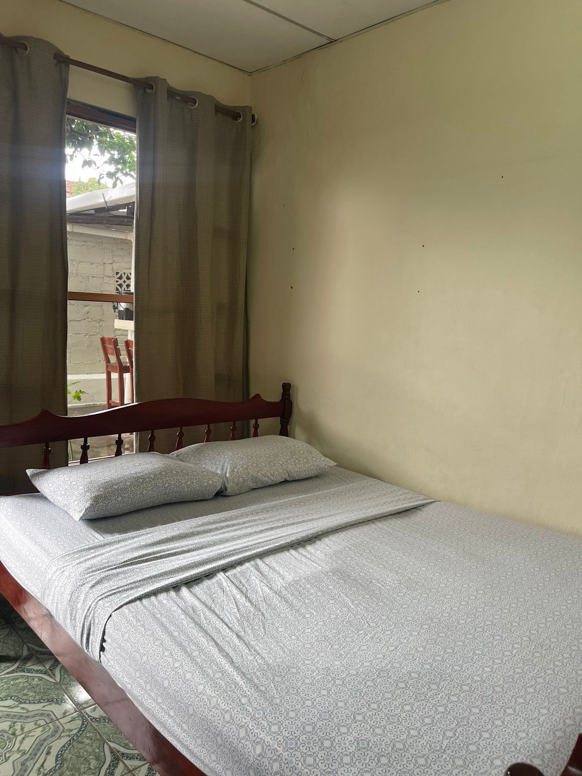 A single bed with a wooden headboard in a room with plain walls and a window with curtains.