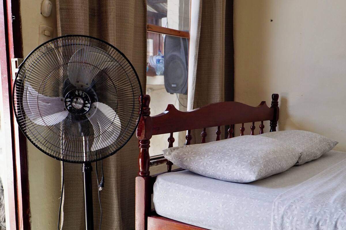 Quarto com uma cama, um ventilador e uma cortina.