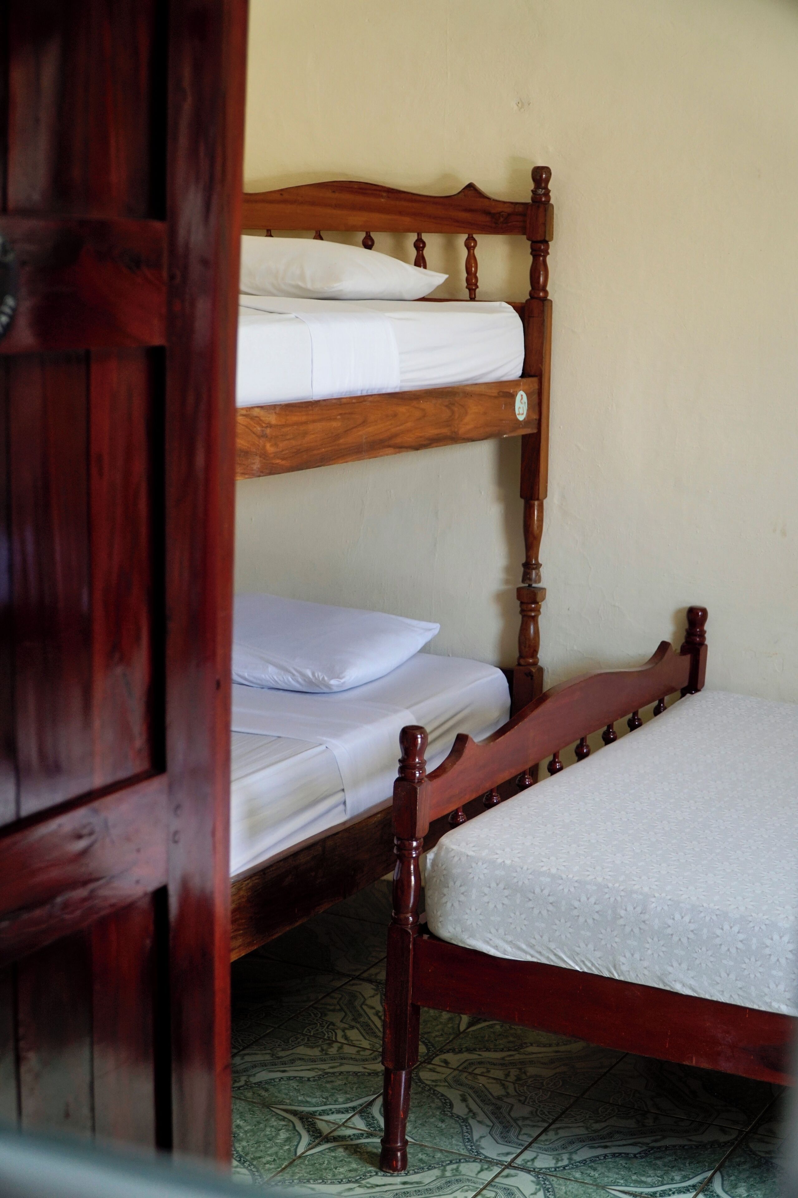 A wooden bunk bed with white bedding in a room with patterned floor tiles.
