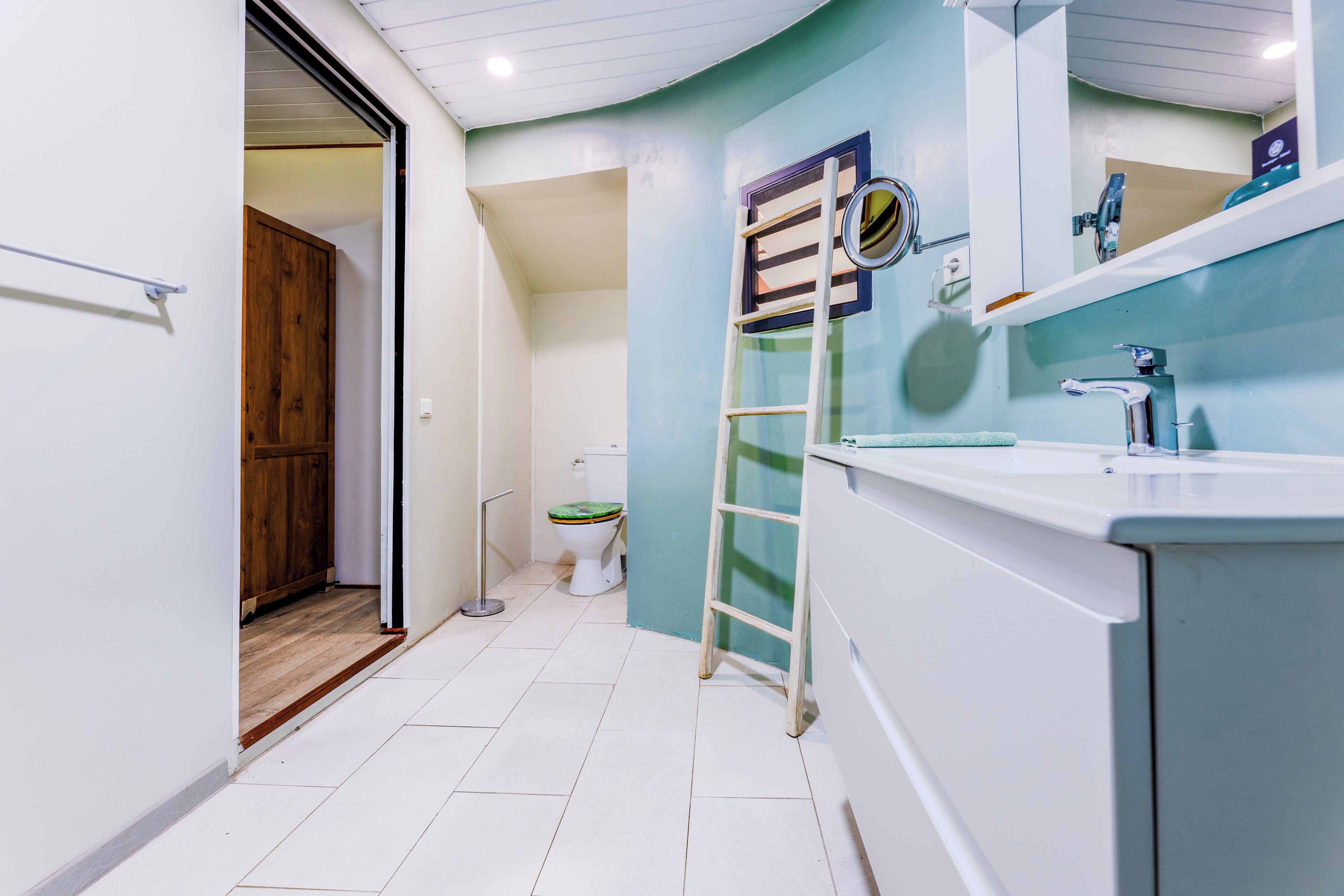 Un baño con inodoro, lavamanos, espejo y puerta de madera.