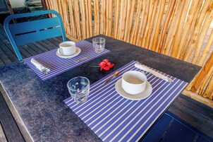 Una mesa con dos tazas blancas y vasos sobre posavasos a rayas azules, una flor roja y una silla azul.