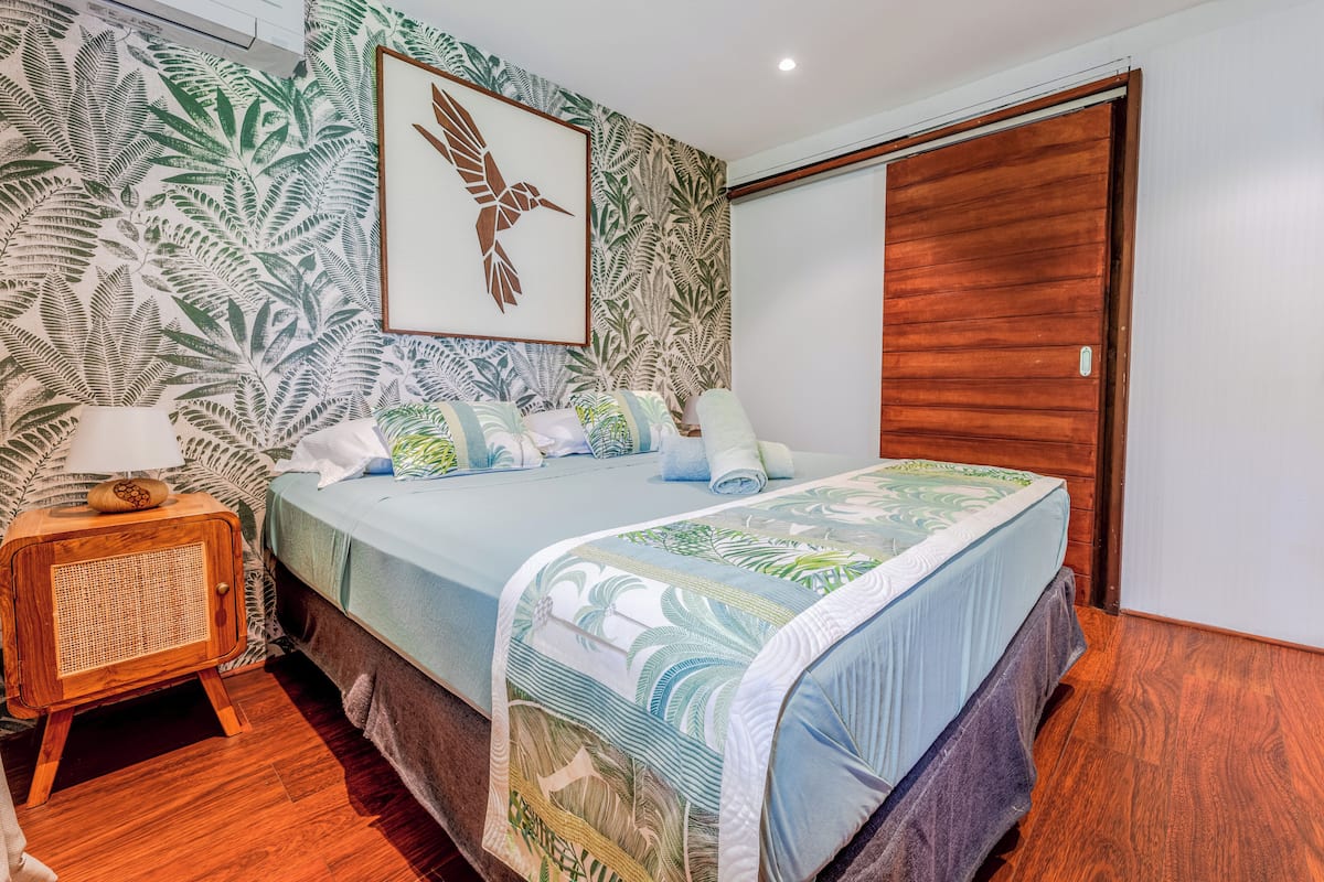 A bedroom with a bed, a wooden nightstand, a framed picture, and a door.
