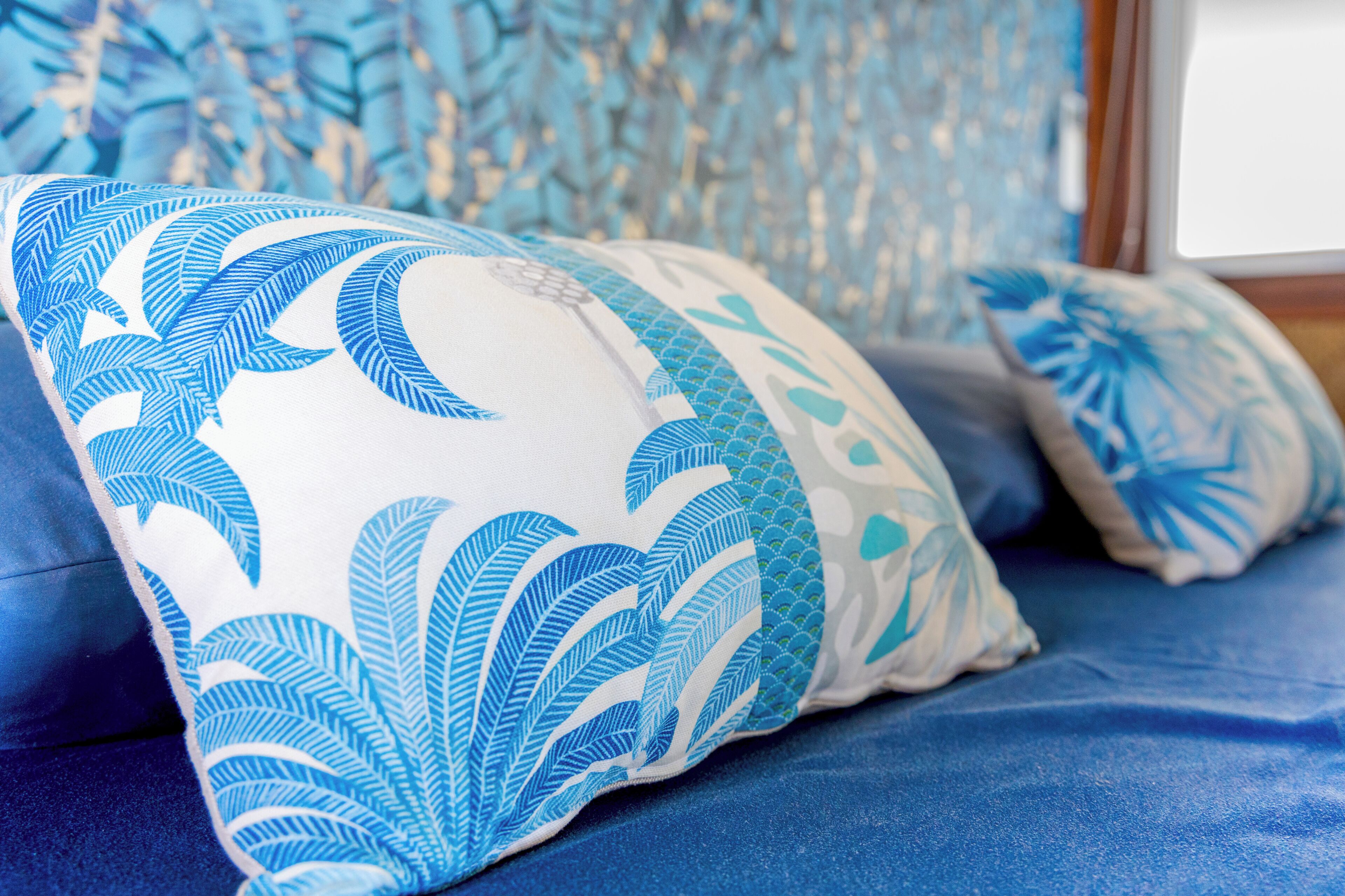 Un lit avec une literie bleue et des coussins décoratifs ornés de motifs de feuilles.