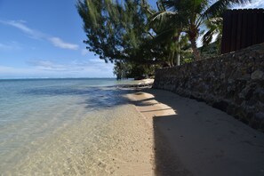 A beach with clear shallow waters, a stone wall, and palm trees. - Fare Aute Beach (Moorea-Maiao)