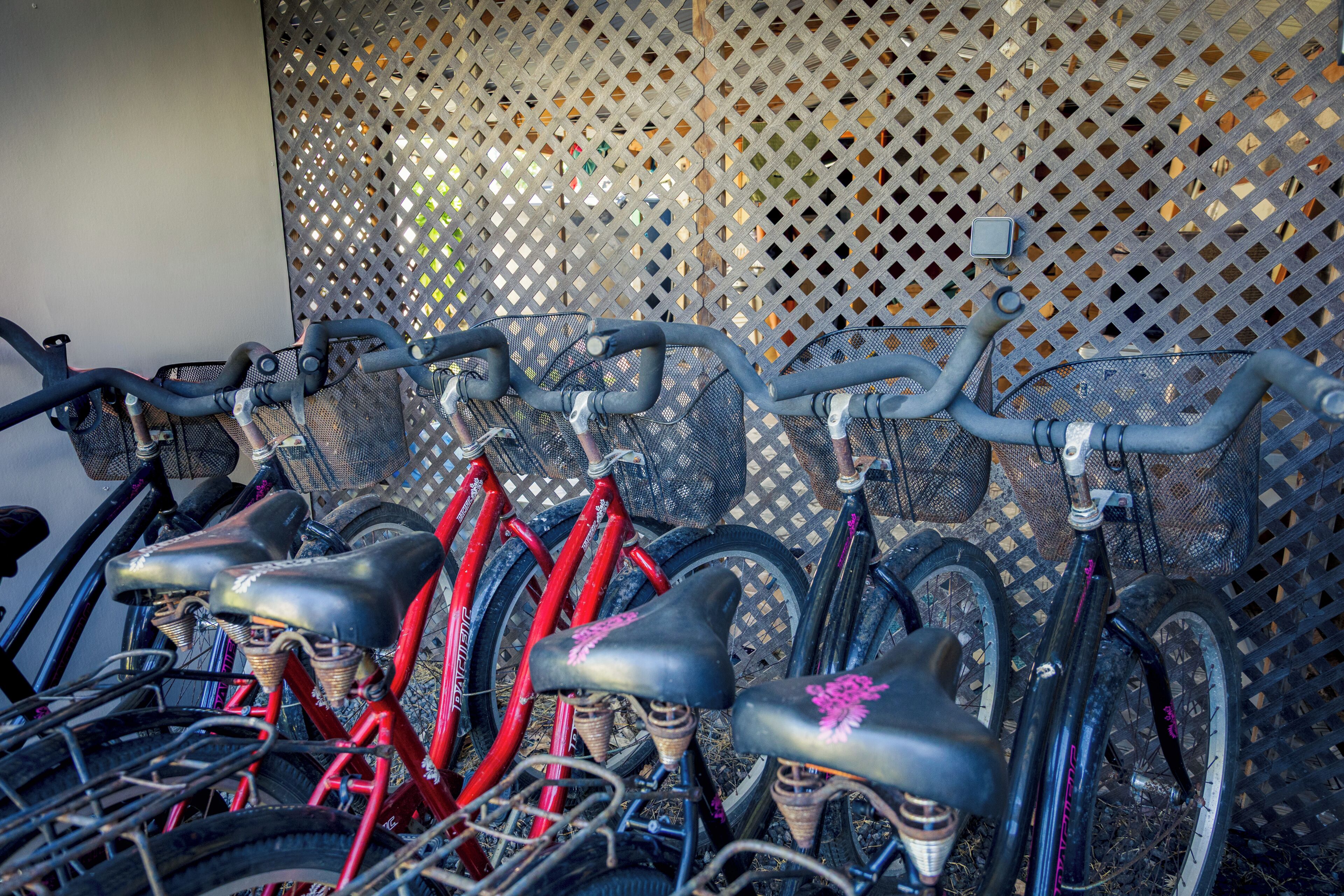 A row of bicycles with baskets, secured to a wall with a lattice pattern.