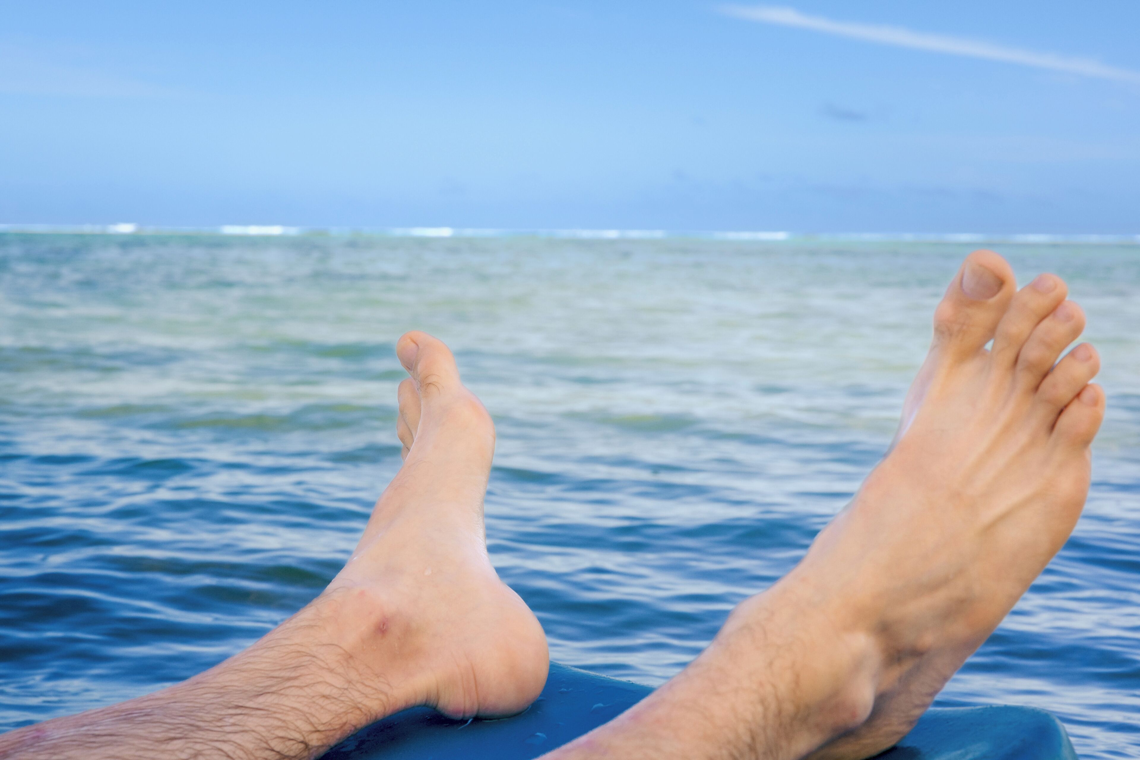 A person's feet resting on a blue surface with a body of water and a distant horizon in the background.