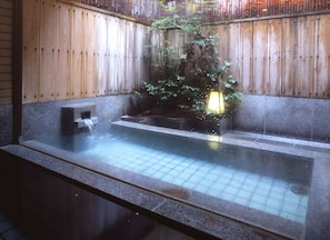 Zona de baños termales con una cerca de madera, una plataforma de piedra y una pequeña cascada.