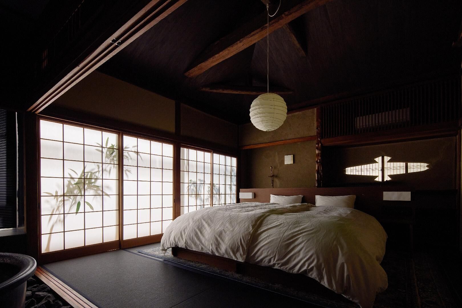 A traditional Japanese-style bedroom with tatami flooring, a large window with bamboo, and a hanging paper lantern.