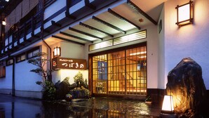 Un edificio japonés tradicional con fachada de madera, un farol de piedra y una fuente en primer plano.