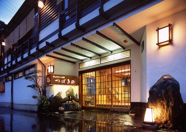 Un edificio japonés tradicional con fachada de madera, un farol de piedra y una fuente en primer plano.