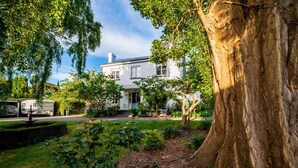 A two-story house with a front porch, surrounded by a well-maintained garden and large trees. - Boscobel of Tasmania (West Ulverstone)