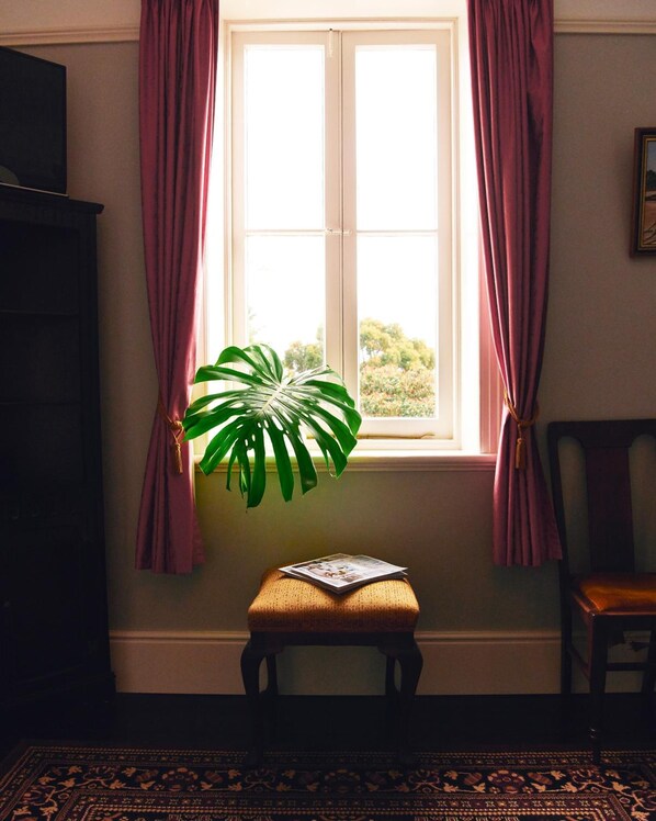 Une pièce avec une fenêtre, une plante en pot, un petit tabouret et une chaise.