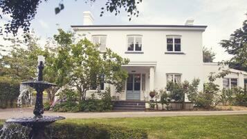 A white two-story house with a front porch, a fountain, and a well-maintained lawn.