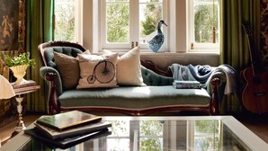 A cozy room with a green upholstered sofa, a glass coffee table, and a window with green curtains. - Boscobel of Tasmania (West Ulverstone)