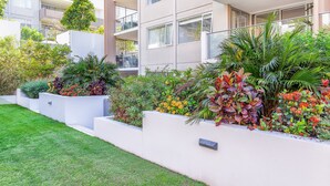 Un edificio moderno con balcones, un césped bien cuidado y diversas plantas coloridas.