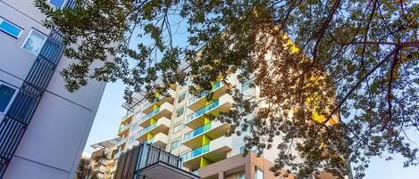 A multi-story residential building with balconies, a gated entrance, and surrounding greenery.
