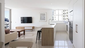 Una cocina moderna con una isla central, un área de comedor con sofá y mesa, y un amplio ventanal con vista a la ciudad.