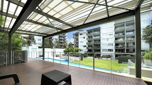 Un espacio al aire libre techado con piscina, suelo de madera y mobiliario exterior.
