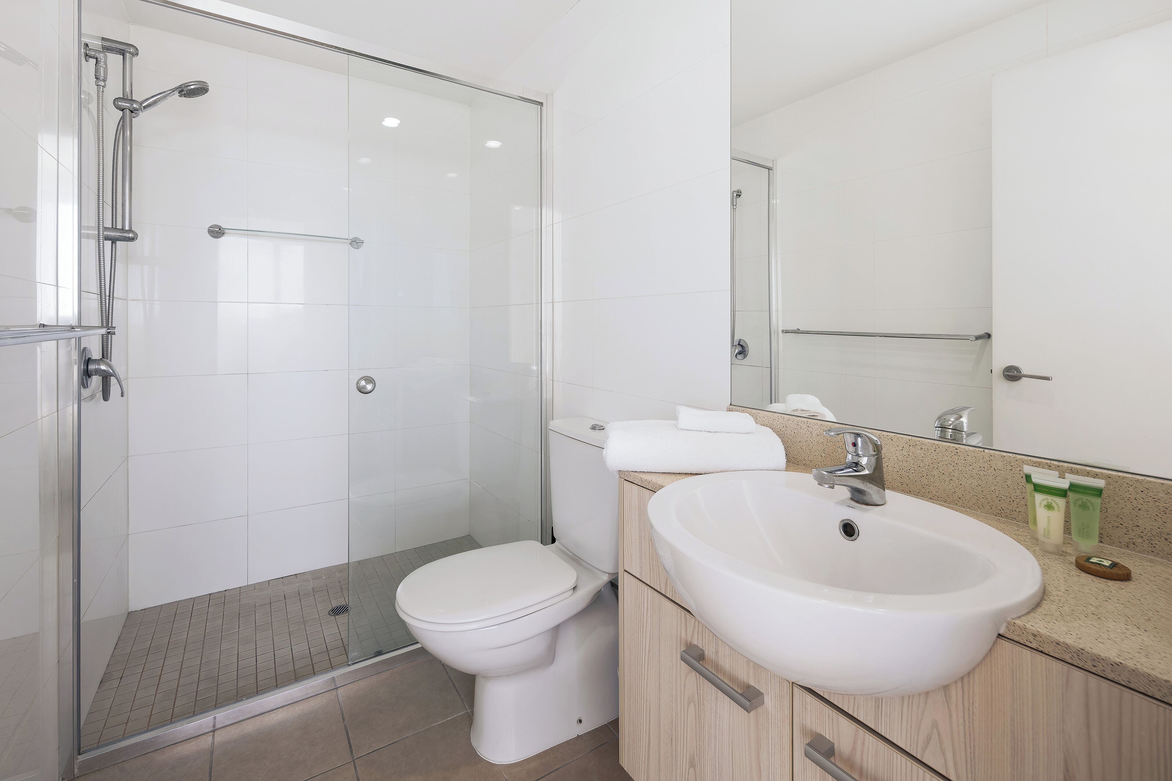 A modern bathroom with a glass-enclosed shower, a white toilet, and a sink with a mirror above it.