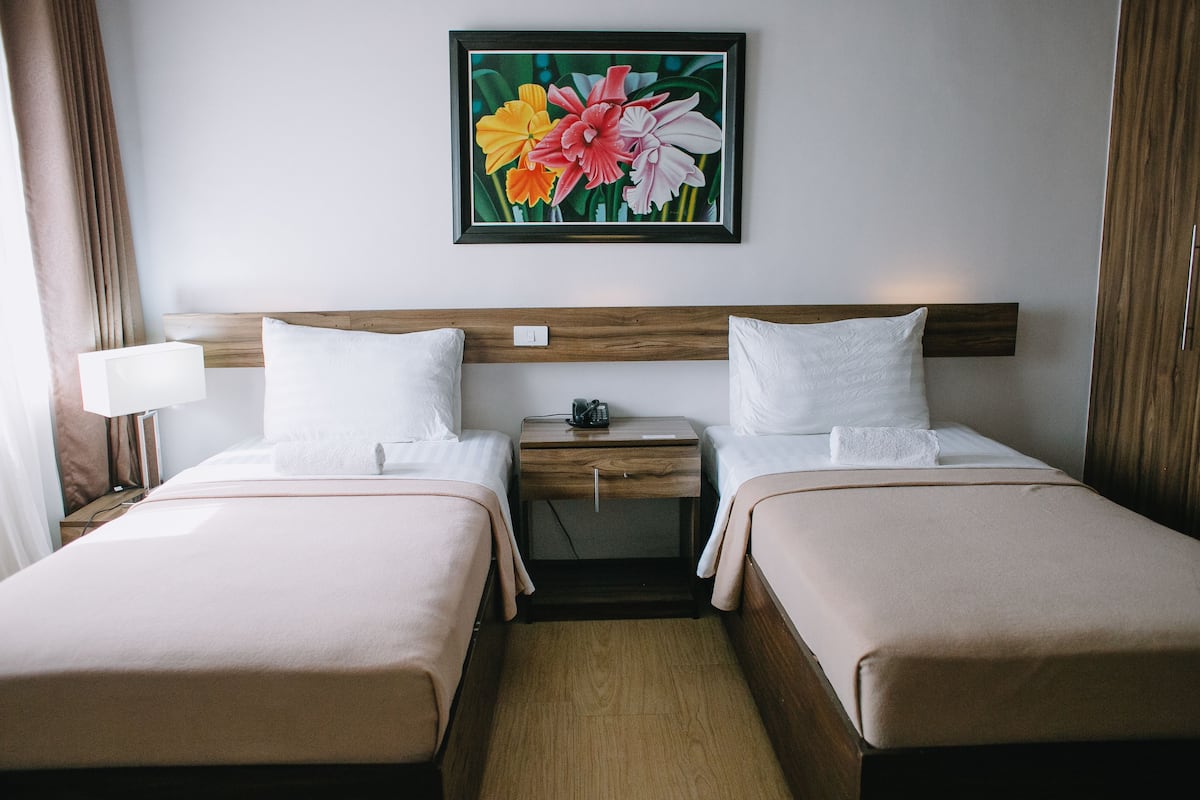 Habitación de hotel con dos camas, una mesita de noche, una lámpara y una obra de arte floral enmarcada en la pared.