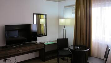 Habitación de hotel con televisión, escritorio, silla, lámpara y ventana con cortinas.