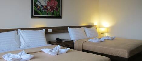 A hotel room with two beds, a nightstand, a lamp, and a framed floral painting on the wall.