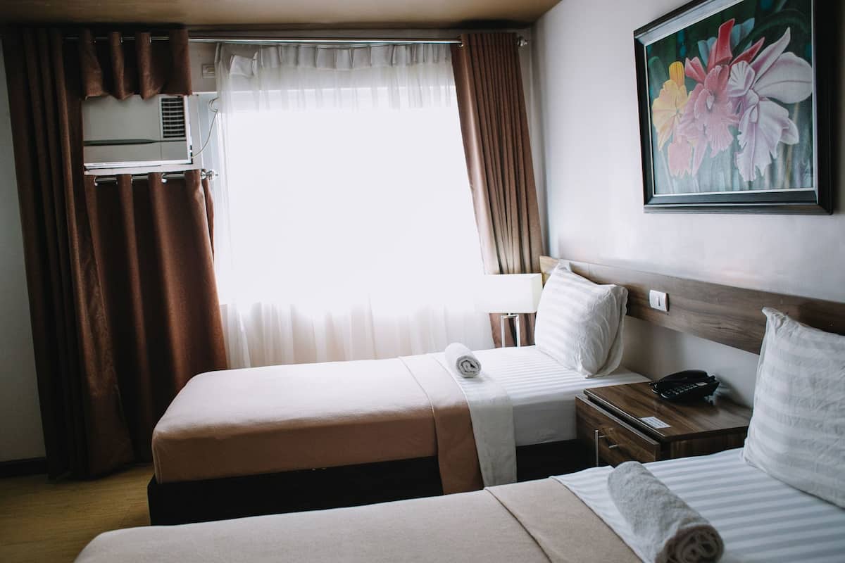 Habitación de hotel con dos camas, un cuadro, un equipo de aire acondicionado y una ventana con cortinas.