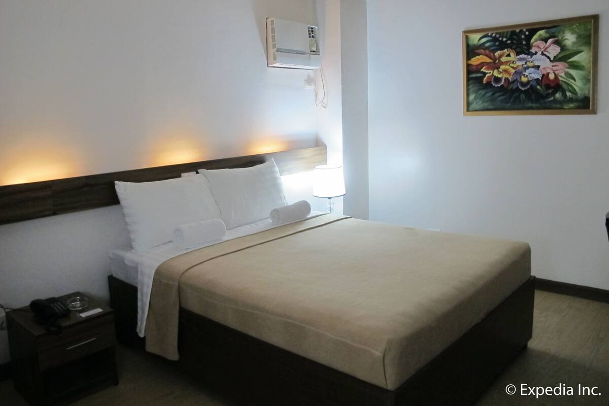 Una habitación de hotel con cama, mesita de noche, lámpara y un cuadro en la pared.