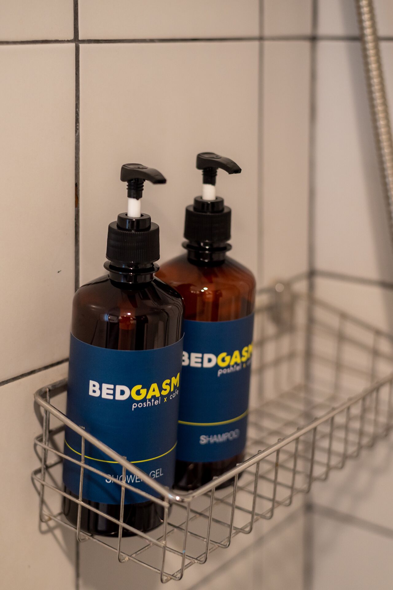 Two bottles of Bedgas shampoo and shower gel in a metal shower rack.